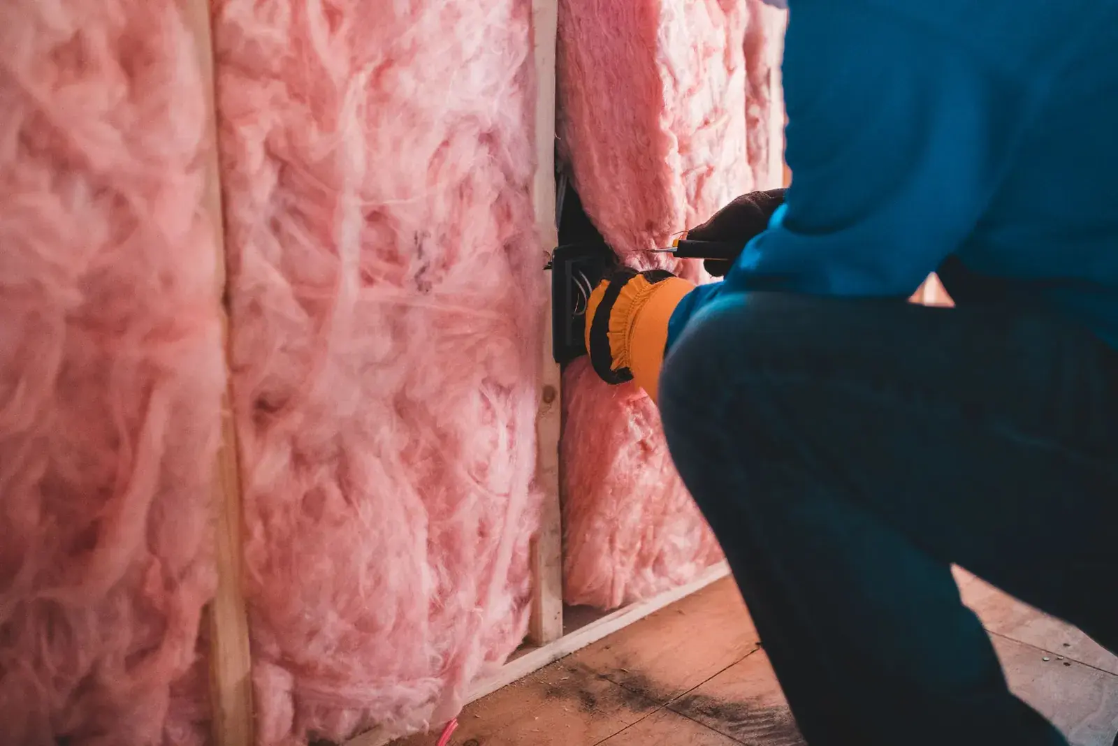 Worker pressing pink insulation between wall framing