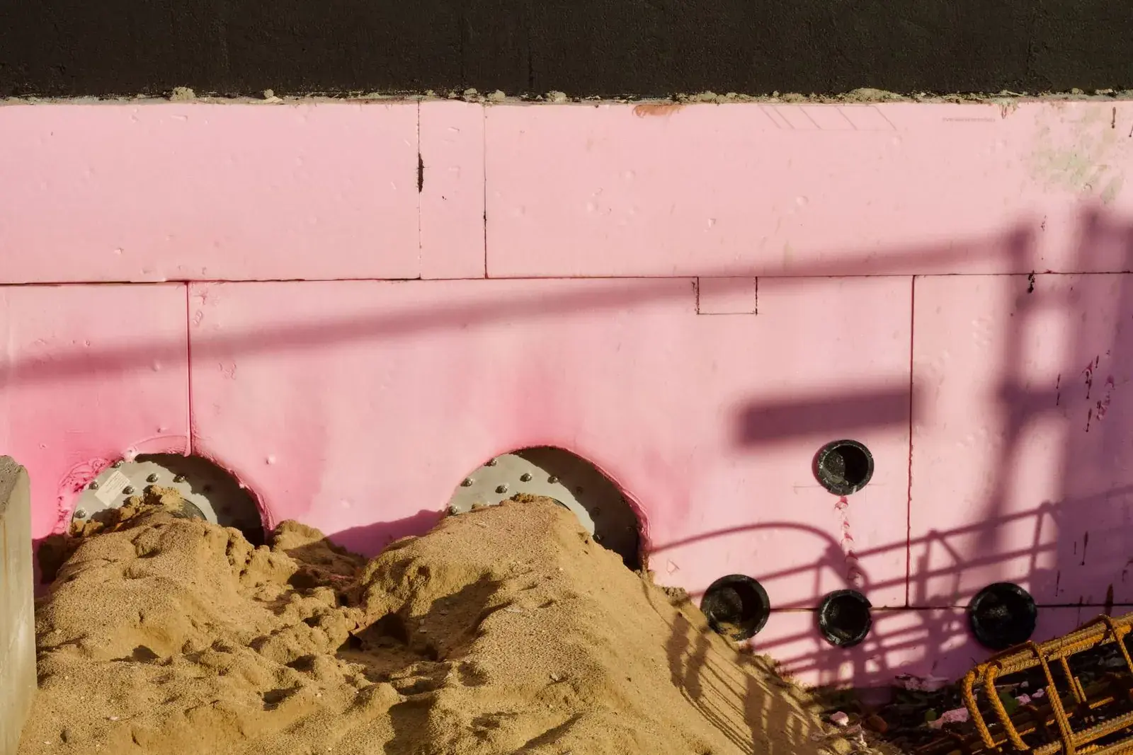 Rigid foam insulation board on a foundation wall above a pile of sand