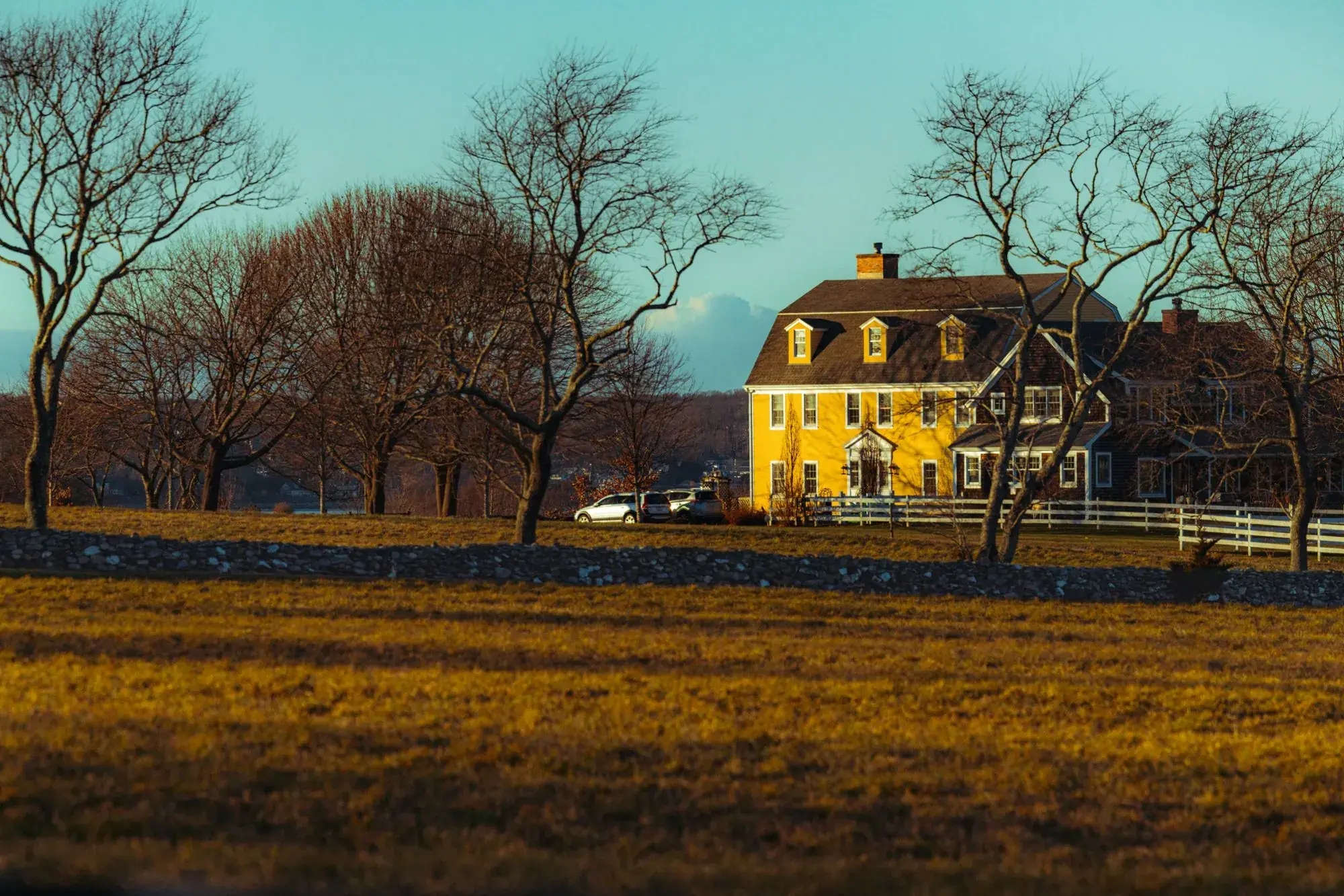 Yellow colonial house across a field at golden hour