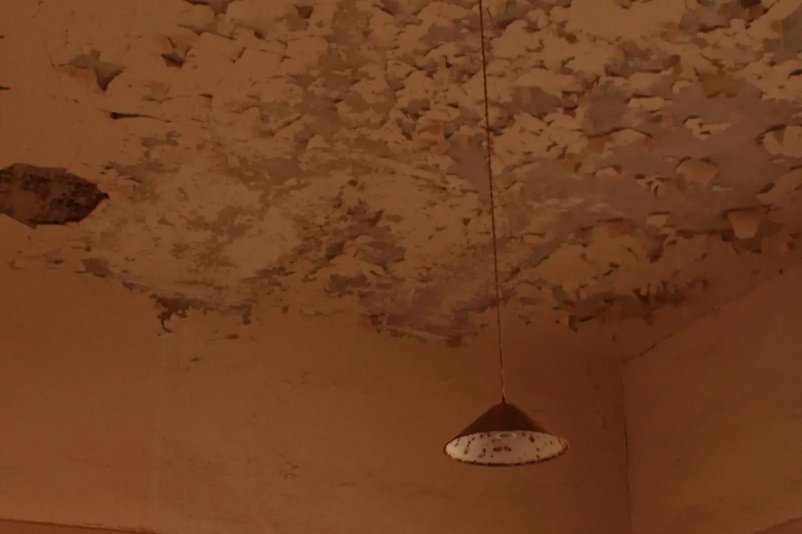 Room corner with a stained, water-damaged ceiling and a hanging lamp